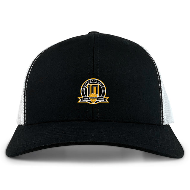 The EMB S&S Activewear Arrows Rugby Club 10th Anniversary Retro Trucker Cap is a black and white hat with a gold-accented circular embroidered front design and snapback closure.
