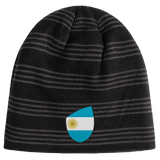 The EMB Canterbury Argentina Shield Beanie features a bold black and grey striped design with an emblem of the Argentine flag.