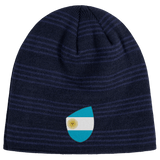 The EMB Canterbury Argentina Shield Beanie is a dark blue striped beanie with an Argentina flag patch featuring a sun emblem, offering warmth and national pride.