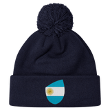 The EMB Canterbury Argentina Shield Pom Pom Beanie in navy blue features a fun patch with a sun-centered flag, adding flair to your winter wardrobe.
