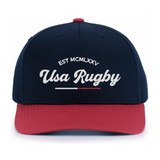 The EMB Augusta USA Rugby Elevated 1975 Eagles Snapback Cap features navy blue and red colors with "EST MCMLXXV Usa Rugby" in white script, ideal for fans who love vintage style and rugby tradition.