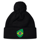 The EMB Canterbury Brazil Shield Pom Pom Beanie features a stylish black design, a charming pom-pom on top, and a vibrant Brazil flag patch on the front.