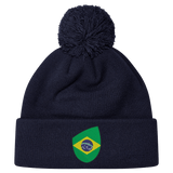 The EMB Canterbury Brazil Shield Pom Pom Beanie in navy blue features a colorful green and yellow patch with a map design, topped with a playful pom pom.