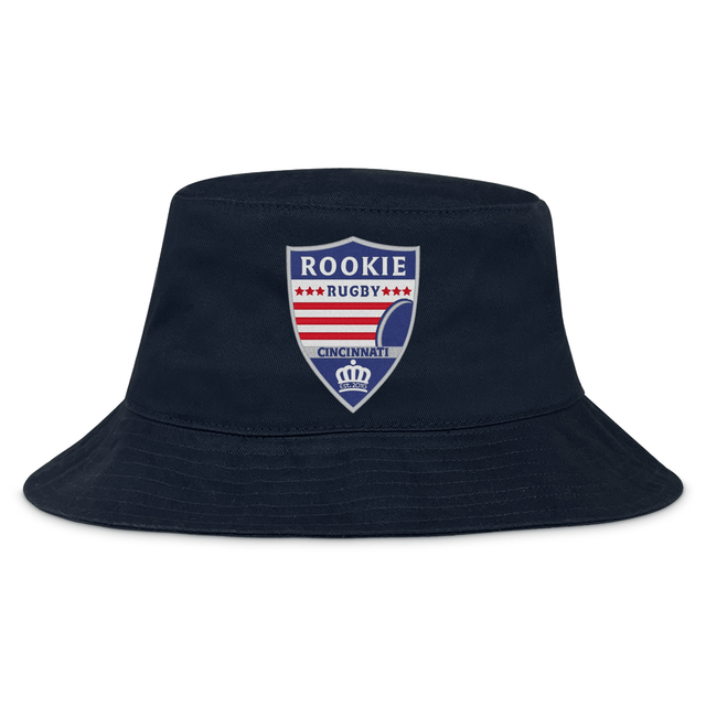 The Cincinnati Rookie Rugby Crusher Bucket Cap by EMB S&S Activewear features durable cotton twill in navy blue and a shield-shaped red, white, and blue "Rookie Rugby Cincinnati" logo on the front for classic style and sun protection.