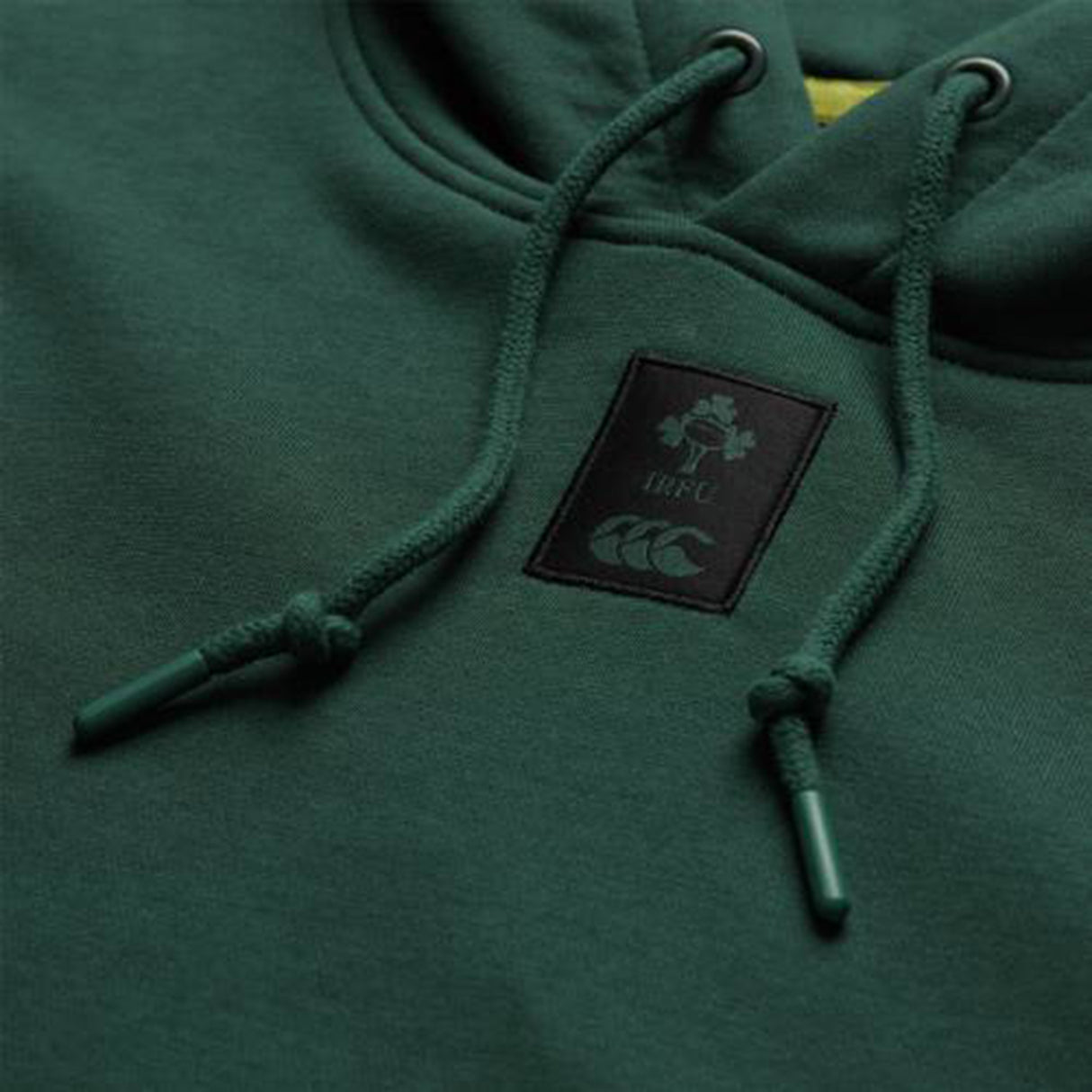 Close-up of the Ireland 26 Leisure Hoodie by Canterbury, featuring a dark green design with a logo patch displaying a shamrock, “IRFU,” and a stylized animal—this leisure hoodie is perfect for fans who value comfort and team spirit.