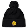The West Chester University Pom Pom Beanie by EMB Canterbury is a black hat with a pom-pom, featuring a yellow and purple circular "West Chester University" patch on the front and a cozy fleece-lined interior for extra warmth.