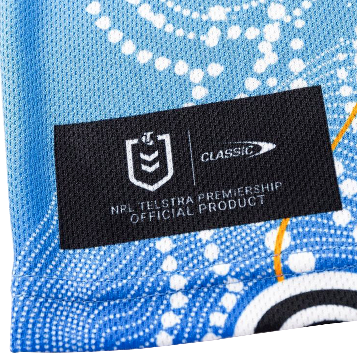 Close-up of a fabric label on the Sharks Indigenous NRL 25/26 Replica Jersey by Classic Sportswear, featuring the NRL Telstra Premiership logo, Classic Sportswear branding, and "Official Product" text on a blue patterned background.