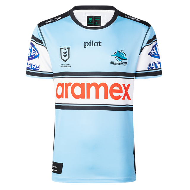 The Sharks NRL 26/27 Replica Home Jersey by Classic Sportswear is light blue with black, white, and blue stripes, featuring the Cronulla Sharks logo, NRL Premiership logo, and "aramex" sponsor across the chest.