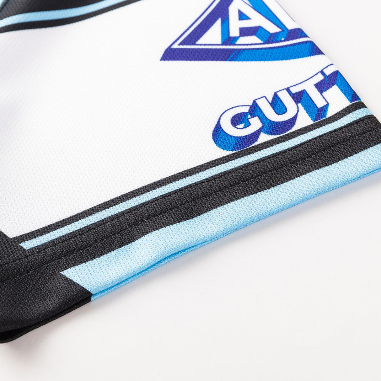 Close-up of the Sharks NRL 26/27 Replica Home Jersey by Classic Sportswear, showing a geometric blue-purple logo, "GUTT" text, and black and blue accents on crisp white fabric.