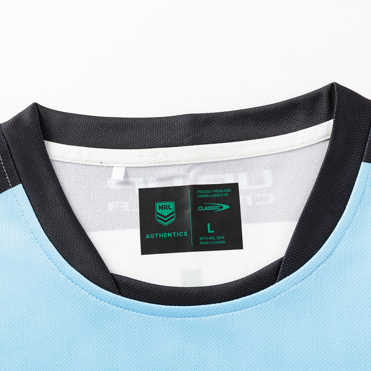Close-up of the neckline and label of the Sharks NRL 26/27 Replica Home Jersey by Classic Sportswear in light blue with black trim, featuring size L, Classic Sportswear branding, and care info.