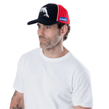 A man in a white t-shirt and a Dolphins NRL 25/26 Media Cap by Classic Sportswear, adorned with black, red, and blue colors and the NRL logo, gazes thoughtfully to the side.