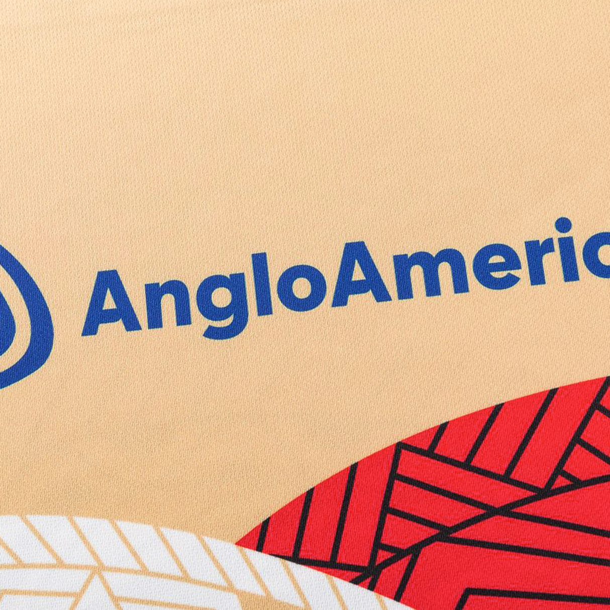Close-up of beige fabric with the blue "AngloAmerican" logo, plus a red geometric-patterned section, from the Dolphins Indigenous NRL 25/26 Replica Jersey by Classic Sportswear.