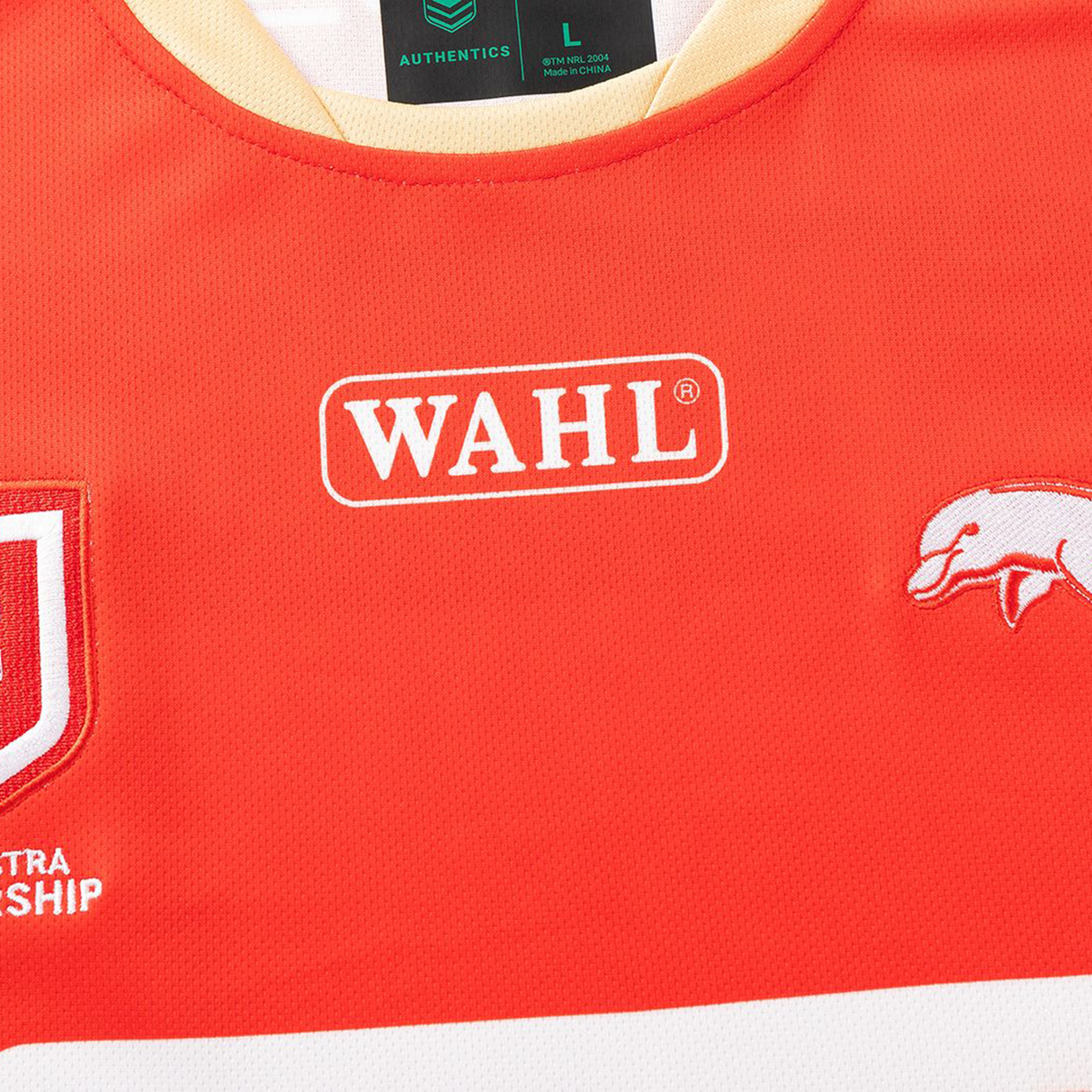 Close-up of the Dolphins NRL 26/27 Replica Home Jersey by Classic Sportswear, showing a red design with WAHL logo, stylized white animal graphic, Classic Sportswear branding, and partial logos.