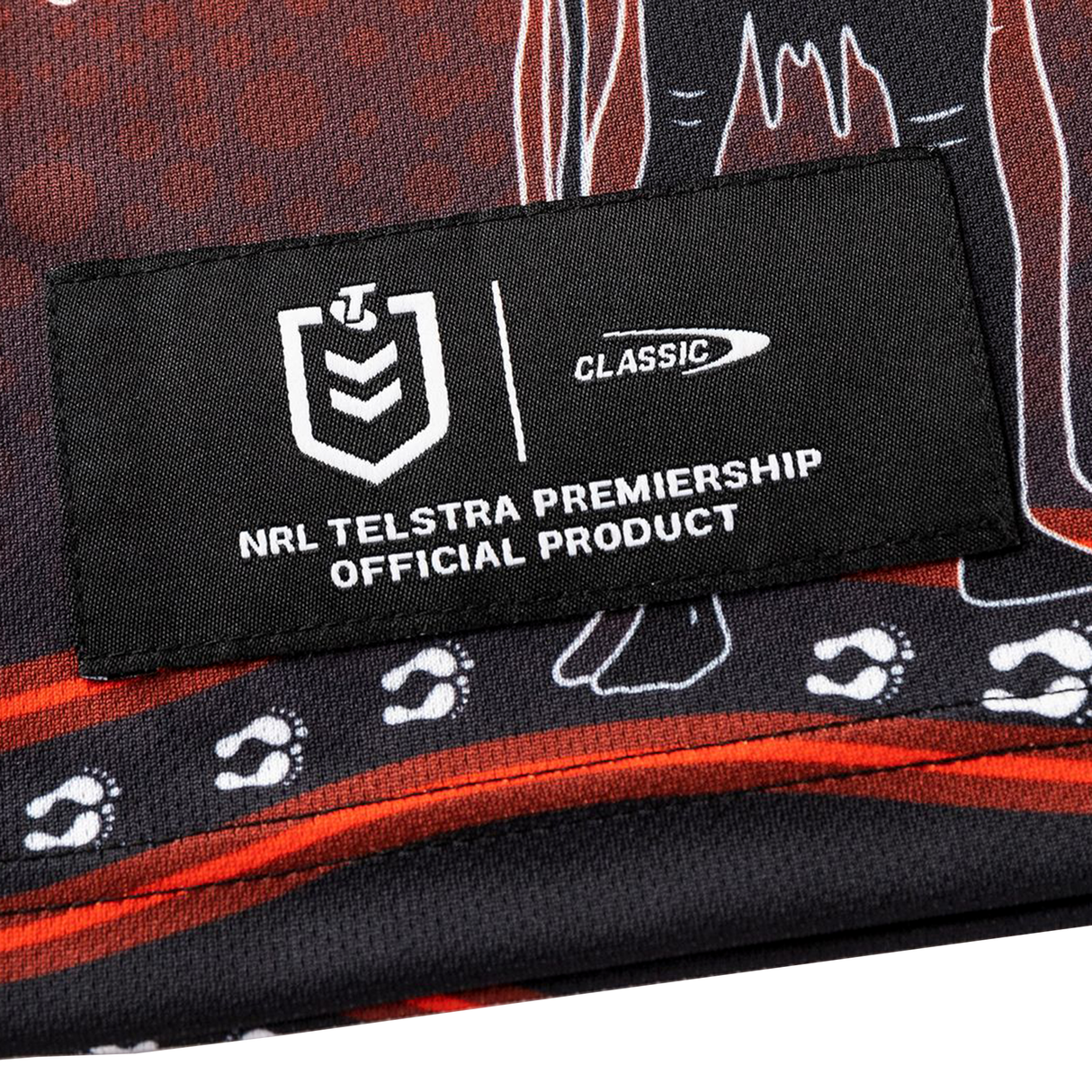 A close-up of a black fabric patch reading "NRL Telstra Premiership Official Product," with white logos and paw prints, featured on the Dragons Indigenous NRL 25/26 Replica Jersey by Classic Sportswear.