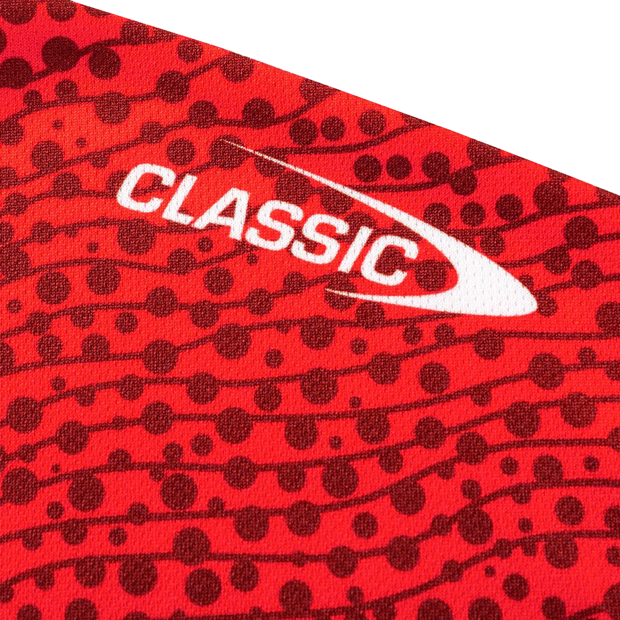 Red fabric with black dots and “CLASSIC” in white beside a swoosh design, inspired by the Dragons Indigenous NRL 25/26 Replica Jersey from Classic Sportswear.