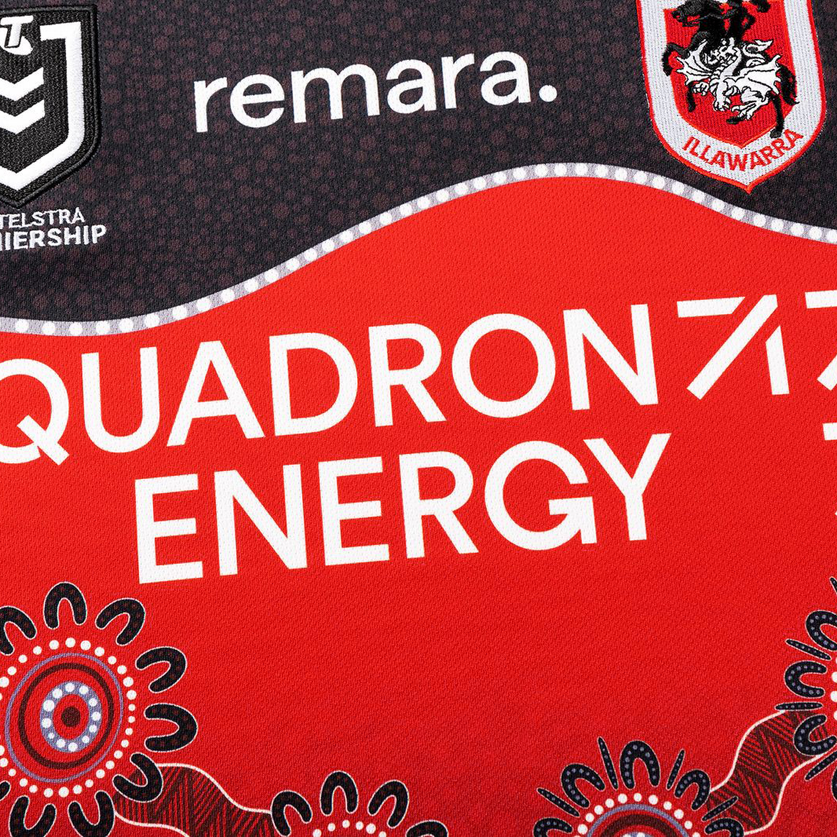 Close-up of the Dragons Indigenous NRL 25/26 Replica Jersey by Classic Sportswear, showcasing QUADRON ENERGY, Telstra Premiership, Illawarra logos, and Indigenous-inspired patterns on a red and black design.
