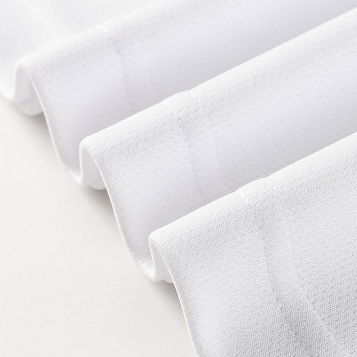 Close-up of four neatly folded edges of white textured fabric, echoing the craftsmanship found in the Dragons NRL 26/27 Replica Home Jersey by Classic Sportswear, arranged in parallel lines on a light surface.