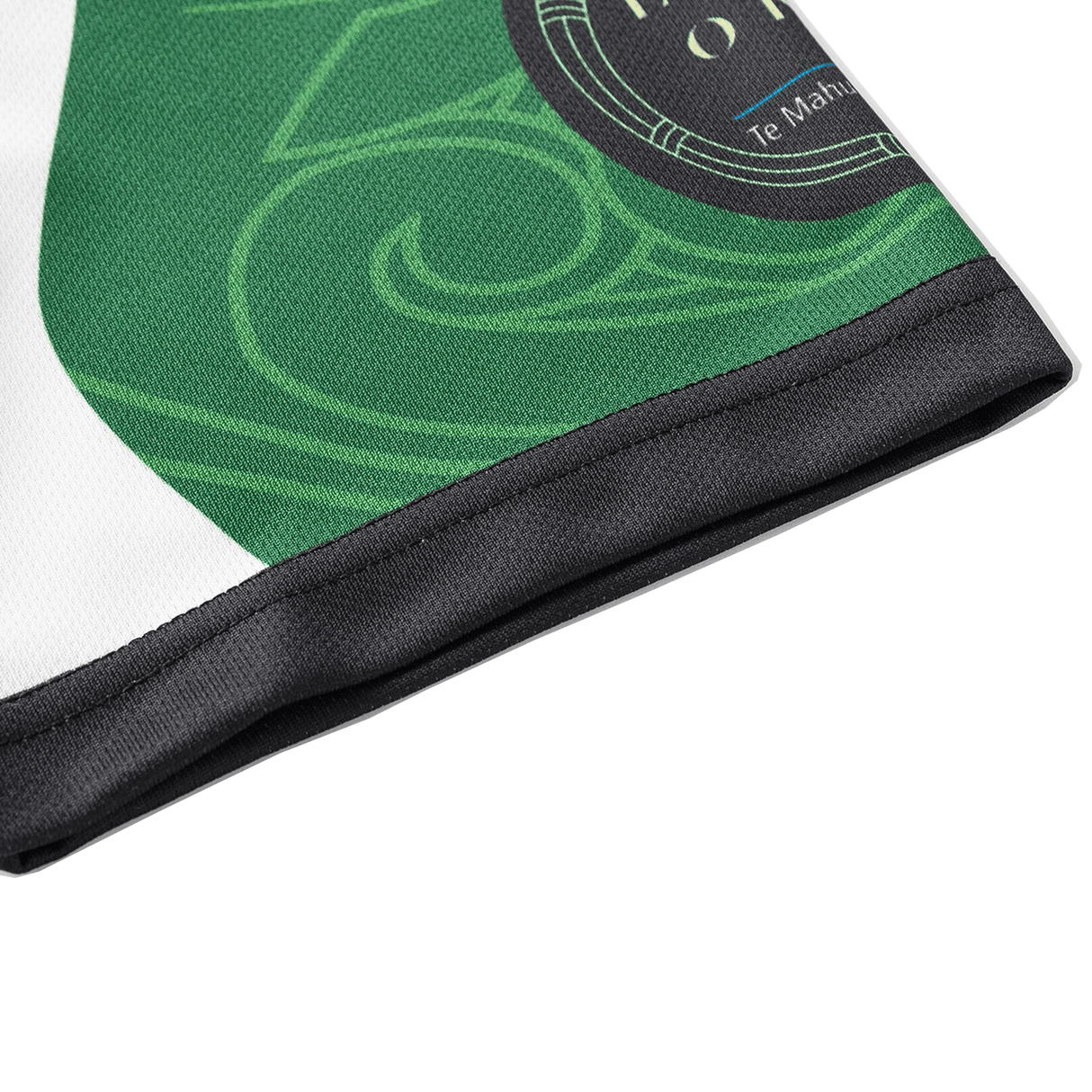 A close-up of a green and black fabric, adorned with sublimated graphics and English/Maori text, resembles the NRL Maori All Stars 25/26 Replica Home Jersey by Classic Sportswear. The material's anti-microbial wickable properties ensure comfort and durability.