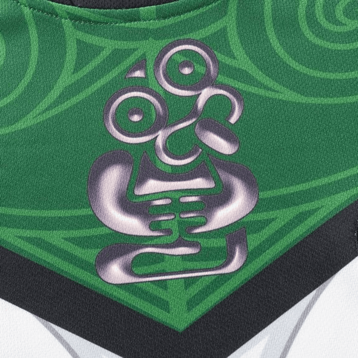 Close-up of the NRL Maori All Stars 25/26 Replica Home Jersey by Classic Sportswear, featuring a green fabric with sublimated graphics and a stylized silver tribal design, blending swirls and geometric shapes.