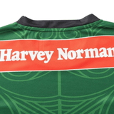 Close-up of the back of a green NRL Maori All Stars 25/26 Replica Home Jersey by Classic Sportswear with a black collar, featuring "Harvey Norman" in white on a red background. The jersey displays vibrant sublimated graphics.