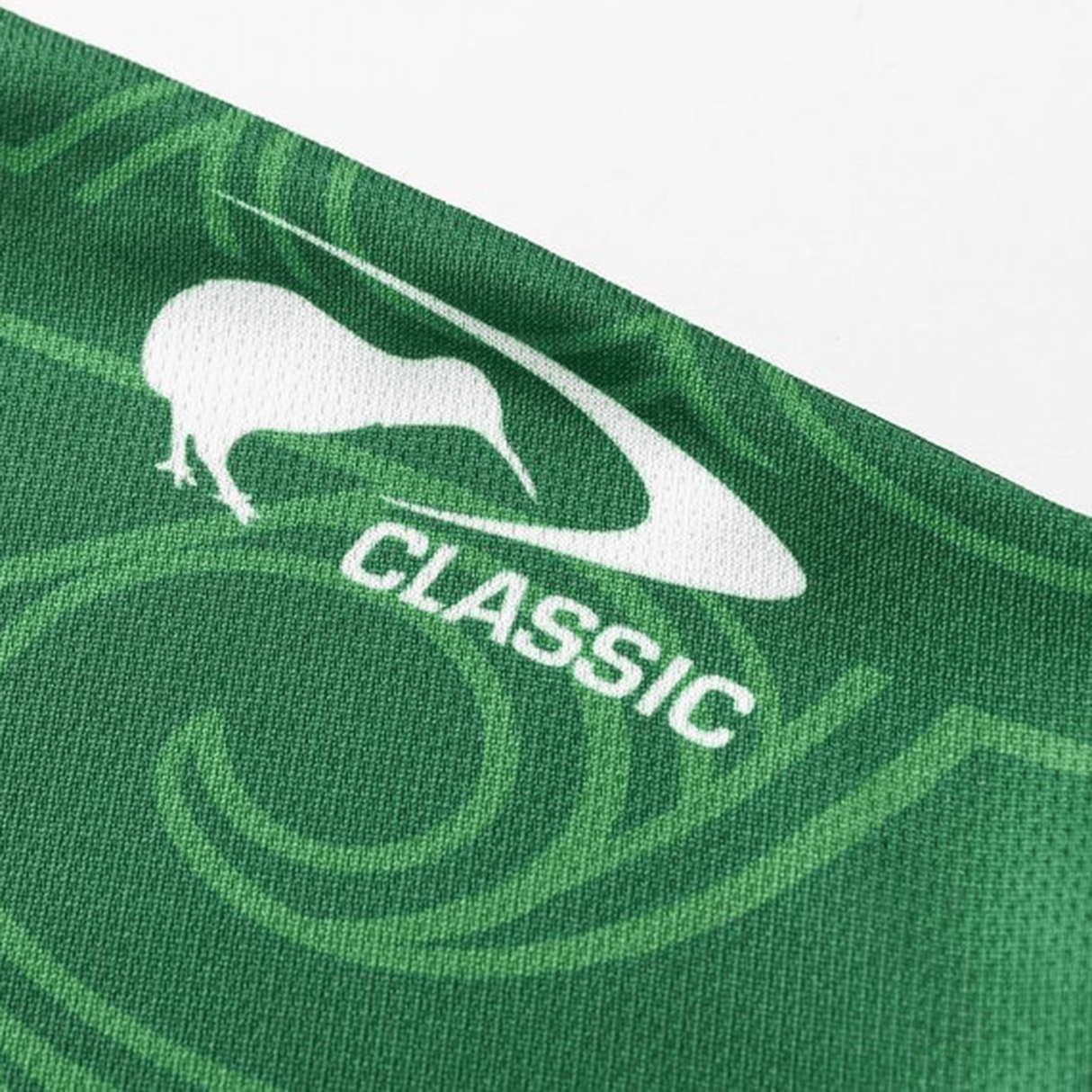 A close-up of the NRL Maori All Stars 25/26 Replica Home Jersey by Classic Sportswear reveals a green fabric with a white kiwi bird silhouette, "CLASSIC," and swirling patterns. Sublimated graphics add depth, while anti-microbial wickable material ensures comfort.