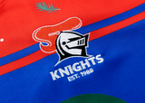 Close-up of a Knights NRL Heritage Jersey by Classic Sportswear with a knight's helmet logo and the text "Knights EST. 1988" embroidered on it, featuring red, blue, and green colors—a timeless tribute to the Newcastle Knights.