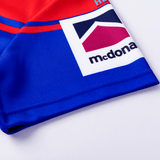 Close-up of a Knights NRL Heritage Jersey by Classic Sportswear featuring a colorful design with red, blue, and white sections, and a prominent logo displaying the word 'mcdona'. This classic sportswear piece echoes the iconic colors of the Newcastle Knights.