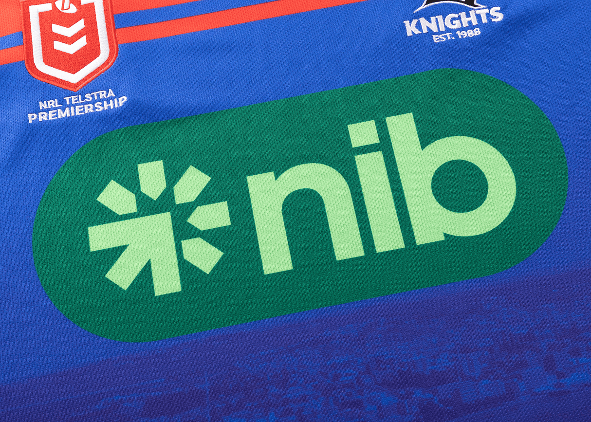 Close-up of a sports jersey featuring the "NRL Telstra Premiership" logo, the "Knights Est. 1988" logo, and a green "nib" logo on a blue background—a true representation of Newcastle Knights’ Knights NRL Heritage Jersey by Classic Sportswear.