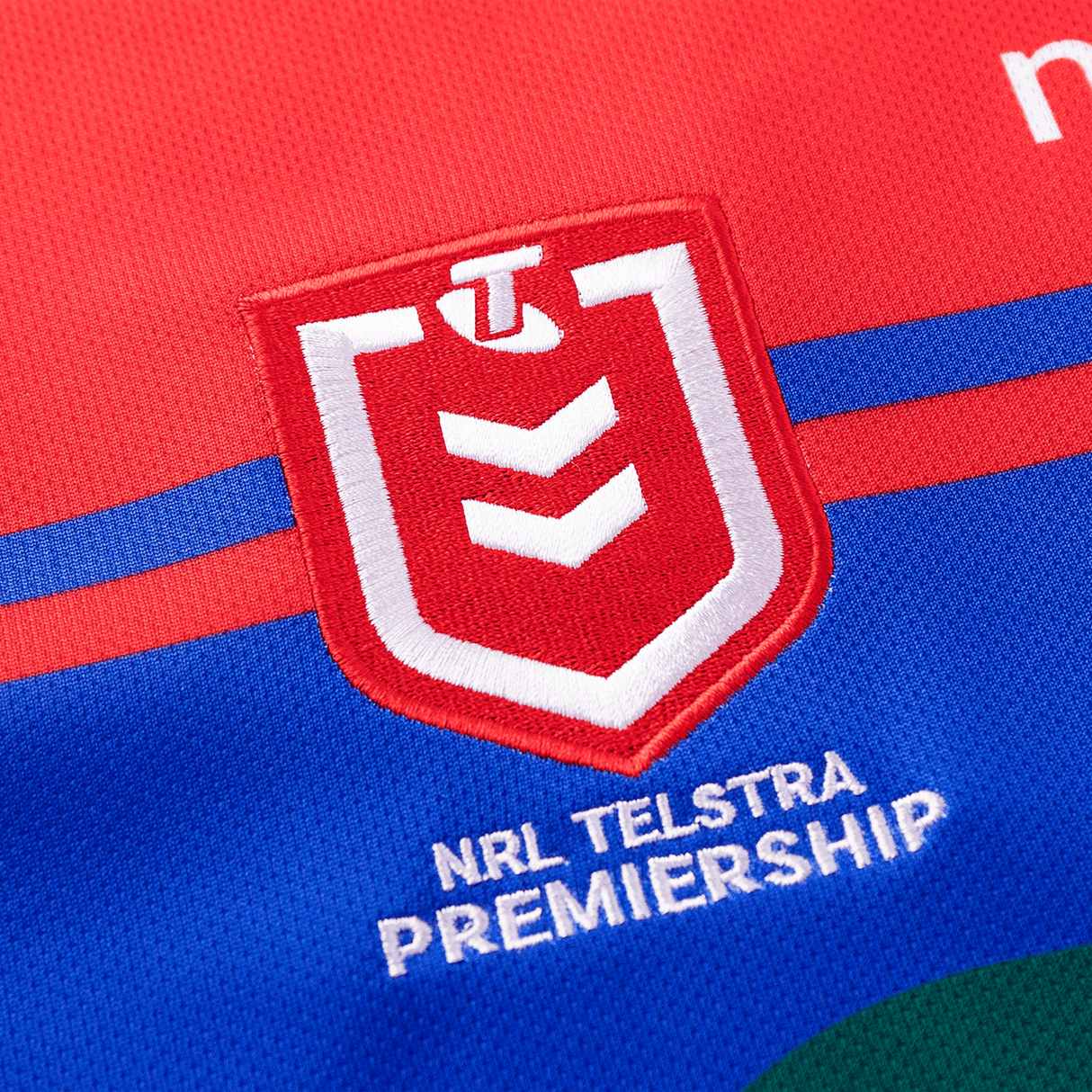 Close-up of a Knights NRL Heritage Jersey by Classic Sportswear showcasing the NRL Telstra Premiership logo, featuring a red and white shield with a 'T' symbol above three downward-pointing chevrons, designed by Classic Sportswear in their Heritage Jersey collection.