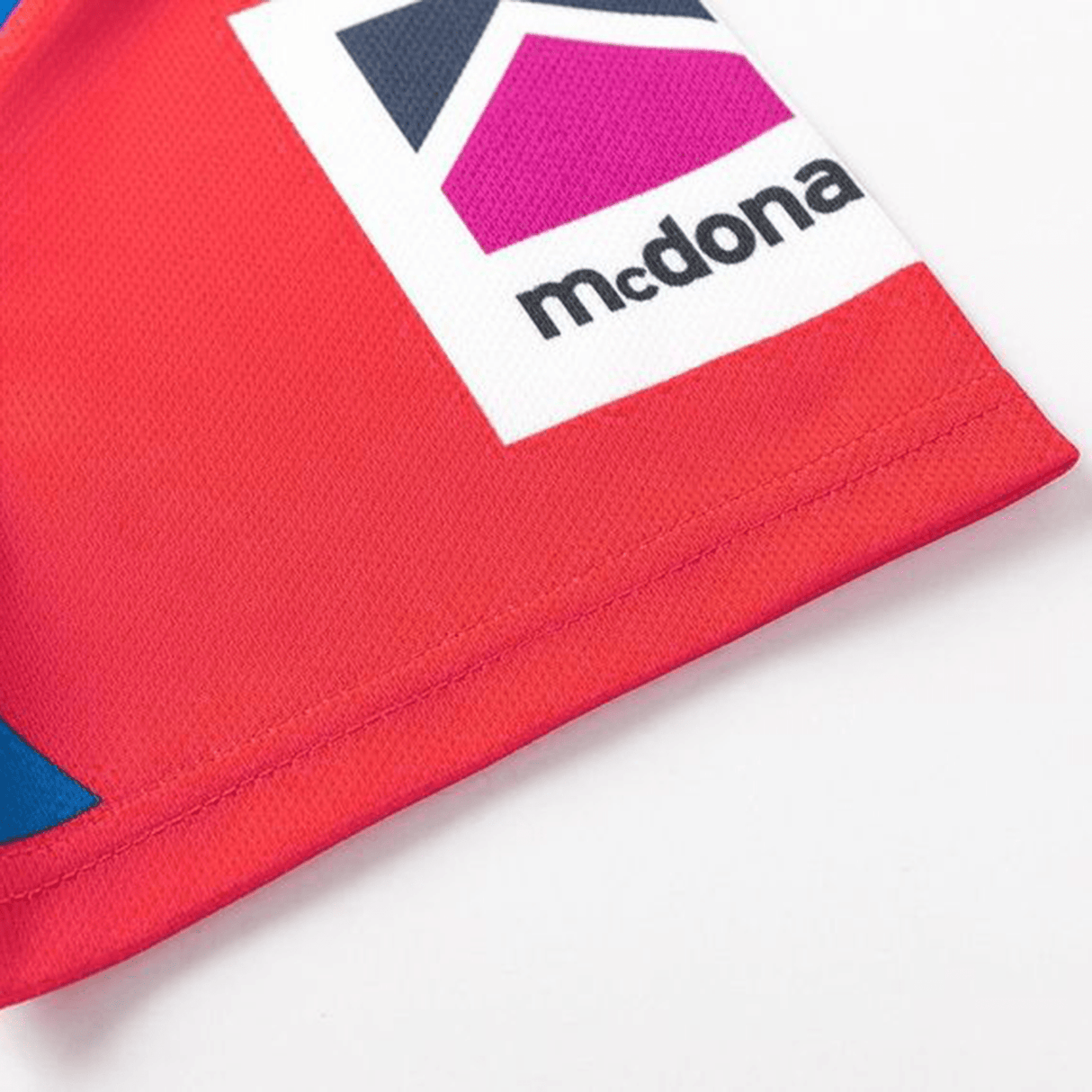 Close-up of a red corner on the Knights NRL 25/26 Replica Home Jersey by Classic Sportswear, showcasing sublimated graphics with a colorful geometric logo and partial text "mcdona." It offers an athletic fit ideal for devoted fans.