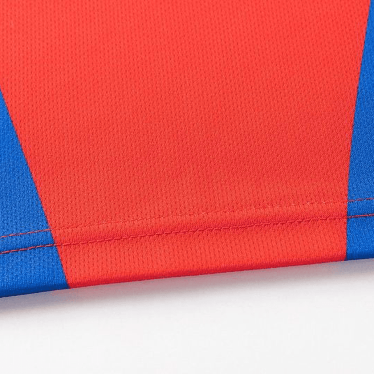 Close-up of a red and blue fabric with a stitched seam, highlighting sublimated graphics. The textured pattern suggests an athletic fit akin to the Knights NRL 25/26 Replica Home Jersey by Classic Sportswear.