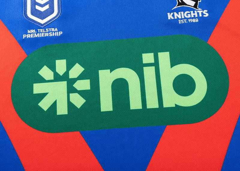 The Knights NRL 25/26 Replica Home Jersey by Classic Sportswear showcases sublimated graphics, featuring the NRL Telstra Premiership and Knights logos. The "nib" logo prominently stands out against a green oval background.