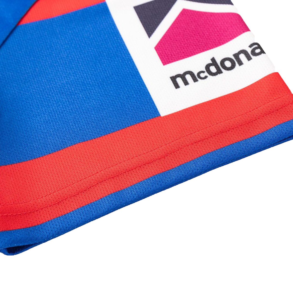 Close-up of a blue, red, and white geometric fabric with partial text "mcdona," from the Knights NRL 26/27 Replica Home Jersey by Classic Sportswear.