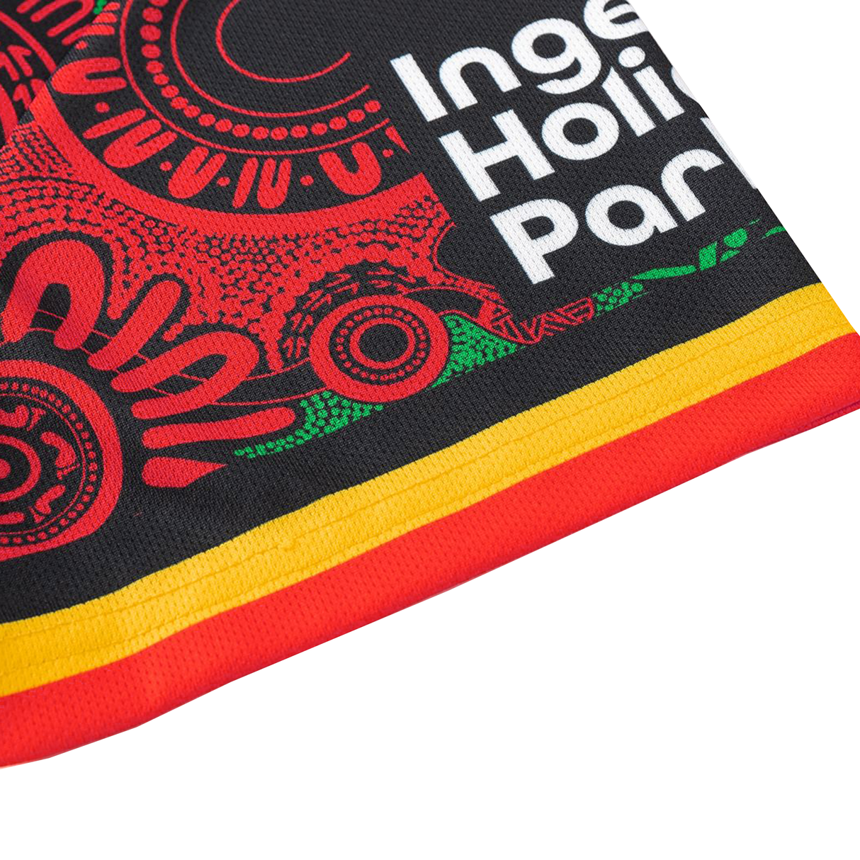 Close-up of fabric with Indigenous-inspired red, green, and yellow patterns, plus partial text "Inge Hoi Par"—a unique detail from the Rabbitohs Indigenous NRL 25/26 Replica Jersey by Classic Sportswear.