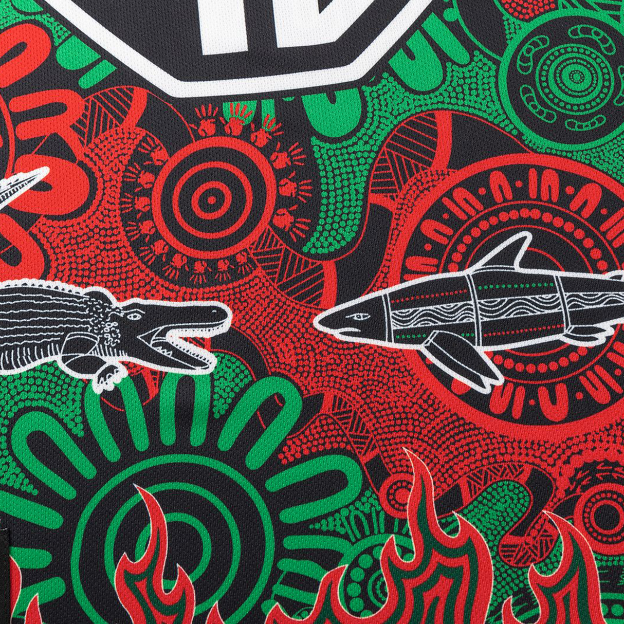 The Rabbitohs Indigenous NRL 25/26 Replica Jersey by Classic Sportswear showcases a vibrant abstract pattern with red, green, and black shades plus crocodile and shark illustrations inspired by Indigenous designs.