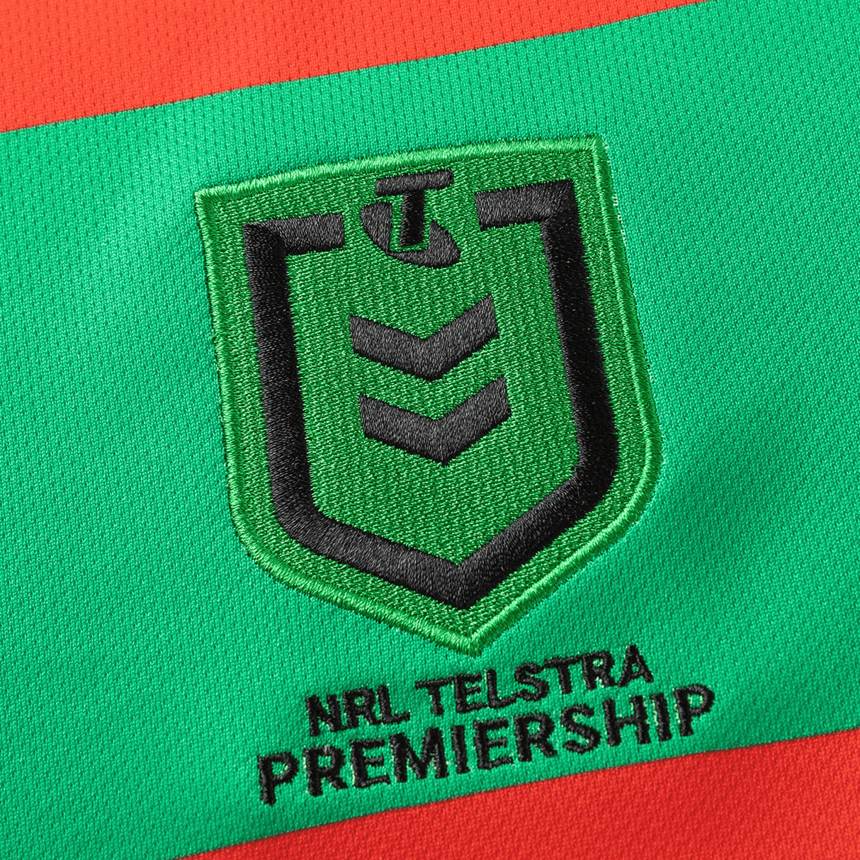 The Rabbitohs NRL 25/26 Replica Home Jersey by Classic Sportswear features an embroidered NRL Telstra Premiership logo on a red and green fabric background, embodying the essence of a Rabbitohs Jersey.
