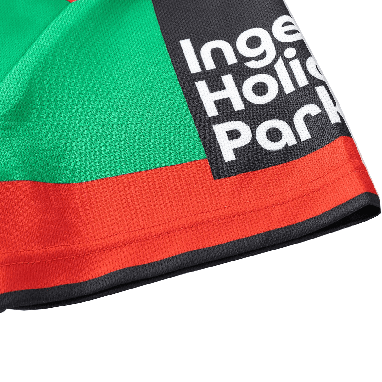 A close-up of a fabric resembling the Rabbitohs NRL 25/26 Replica Home Jersey by Classic Sportswear, displaying black, red, and green sections with partial white text "Inge Holin Par.