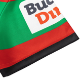 Close-up of green, red, and black fabric showing part of a printed label with "Buc" and "Din"—a detail from the Rabbitohs NRL 26/27 Replica Home Jersey by Classic Sportswear.