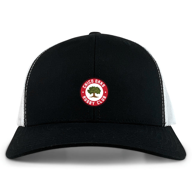 The Chico Oaks Retro Trucker Cap by EMB S&S Activewear features a black and white design, circular "Chico Oaks Rugby Club" embroidery with an oak tree on the front, and an adjustable snapback closure.