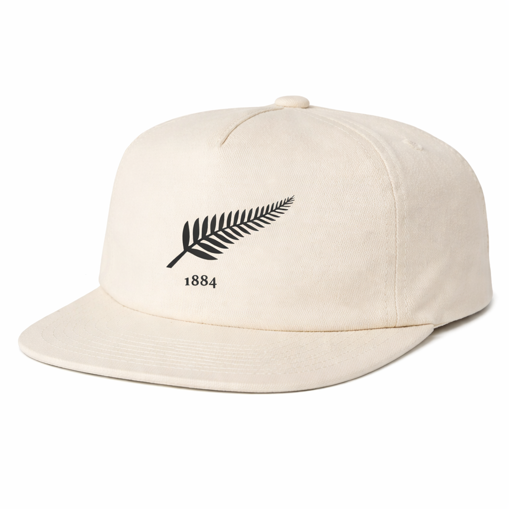 The EMB Weld Nations of Rugby New Zealand Vintage Brushed Cotton Cap is a beige snapback hat with a black fern leaf and "1884" on the front, inspired by vintage NZ rugby caps for a comfortable, adjustable fit.