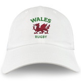 The Nations of Rugby Wales Dad Cap by EMB S&S Activewear is a white cotton hat embroidered with "WALES RUGBY" in green and a bold red Welsh dragon—perfect for fans.