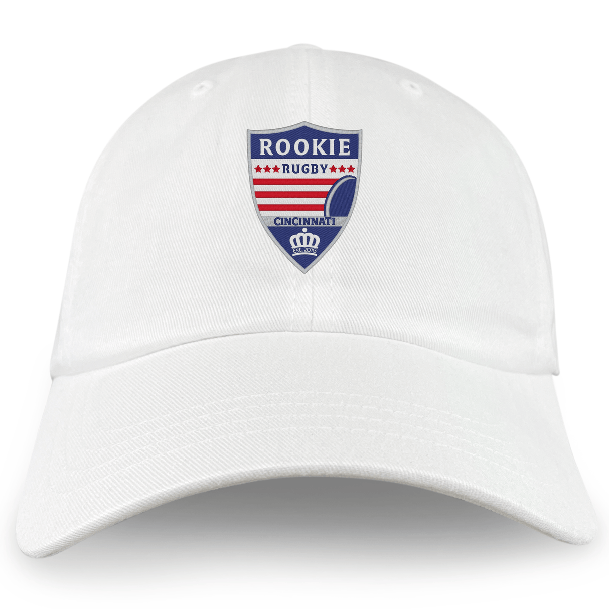 Introducing the Cincinnati Rookie Rugby Adult Low-Profile Cotton Twill Dad Cap by EMB Alpha Broder. This white cotton twill baseball cap features a "Rookie Rugby Cincinnati" logo with red, blue, and white colors, a rugby ball graphic, and a small crown at the bottom. This stylish dad cap showcases embroidered team branding for an added touch of sophistication.