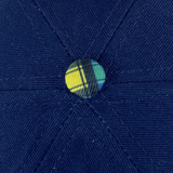 Close-up of 100% organic cotton fabric in blue from Ellis Rugby Doddie Weir Scotland Cap, featuring stitched sections merging at a central, plaid-covered button.