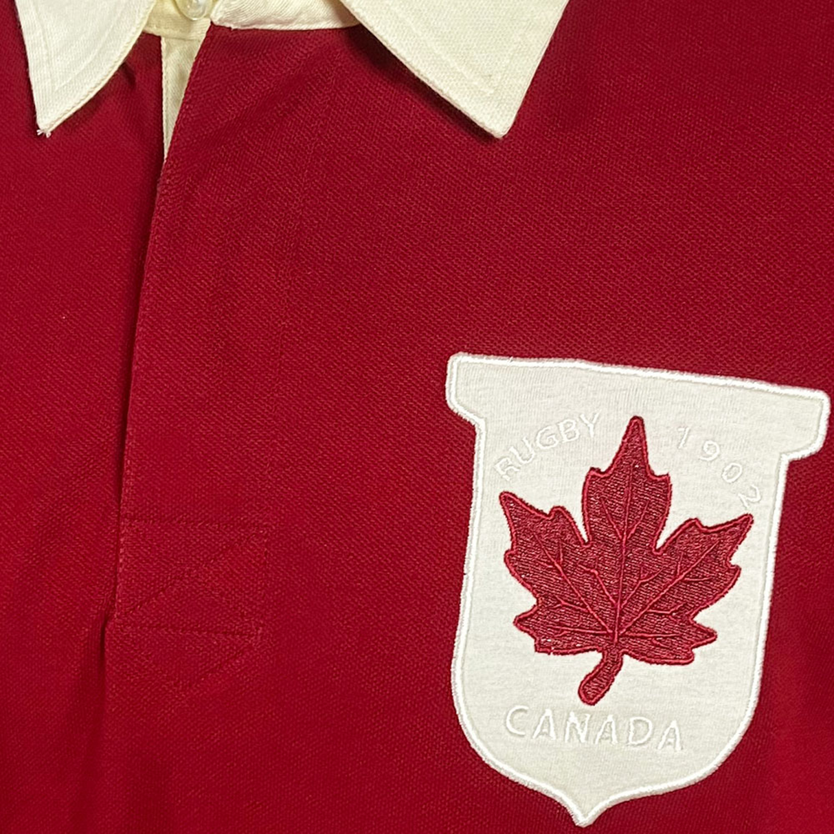 Close-up of the Ellis Rugby Canada Rugby Polo, a red shirt with a white collar and vintage Canadian crest patch featuring "RUGBY 19 02 CANADA" and a red maple leaf, echoing the classic Ellis Rugby style.