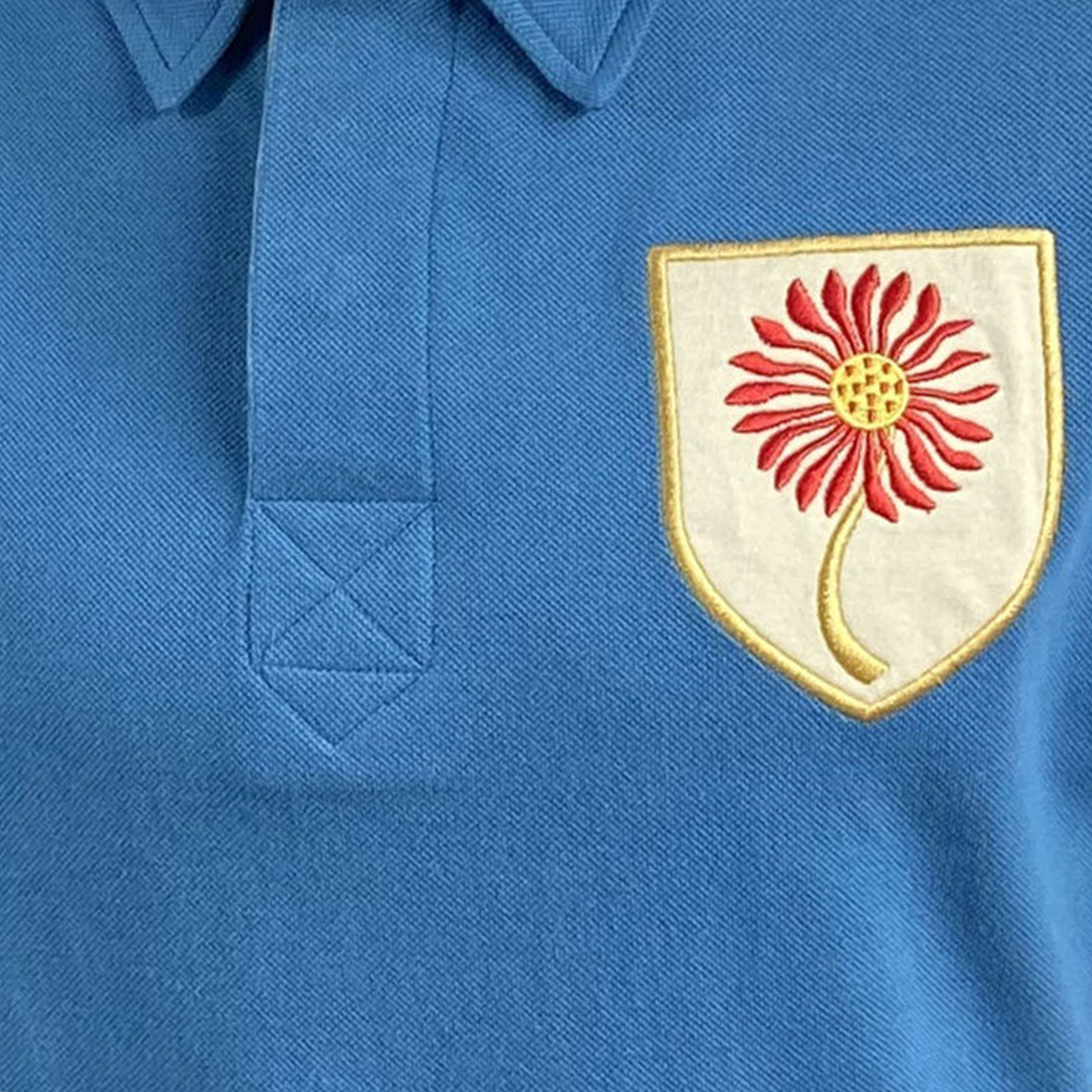 The Northern Transvaal Bulls Vintage Polo by Ellis Rugby showcases a blue shirt with a yellow-edged shield and a red flower emblem on the chest, echoing Ellis Rugby's classic Northern Transvaal style.
