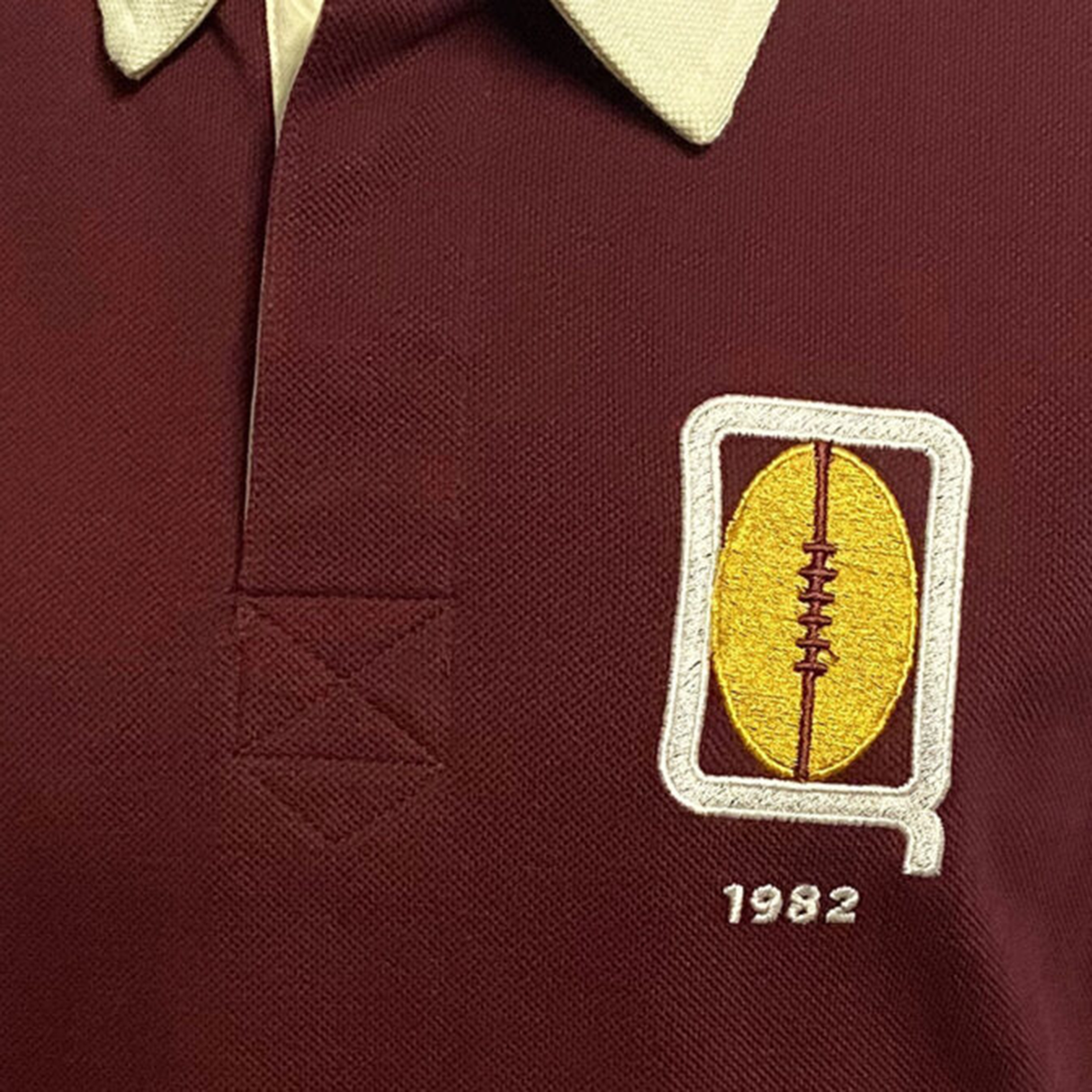 The Ellis Rugby Queensland 1982 Vintage Rugby League Polo highlights a maroon shirt with a beige collar featuring an embroidered yellow football and "1982," celebrating Queensland Rugby League's State of Origin era.