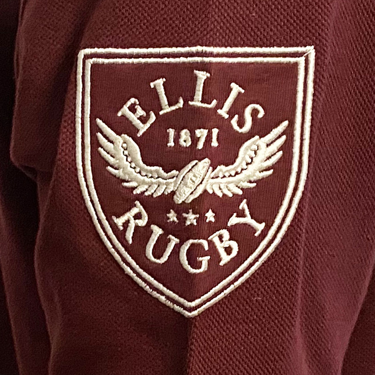 A maroon fabric polo with a white embroidered emblem featuring "Ellis Rugby" and "1871," a winged rugby ball, and three stars, evoking Queensland Rugby League history. This is the Queensland 1982 Vintage Rugby League Polo by Ellis Rugby.