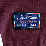 A label on maroon fabric reads "Queensland 1982 Vintage Rugby League Polo by Ellis Rugby," inspired by Queensland Rugby League history, with green, white, and red accents that echo the vintage style.