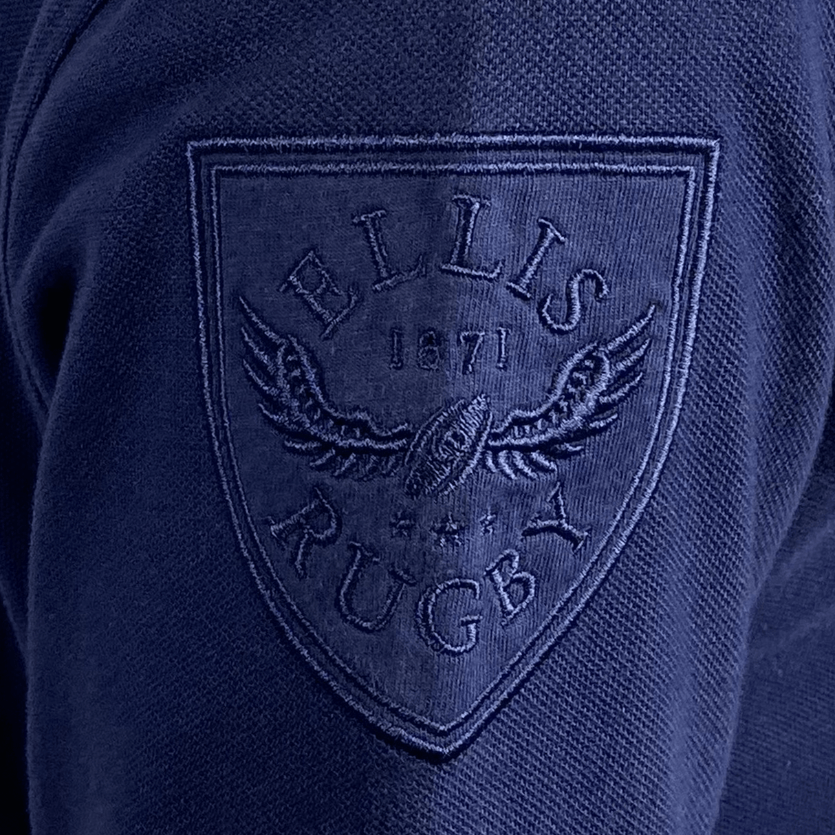 Close-up of the Ellis Rugby Doddie Weir Classic Jersey, showcasing navy blue fabric with an embroidered "Ellis Rugby 1871" shield logo featuring a rugby ball and wing design, and accented by a subtle tartan trim.