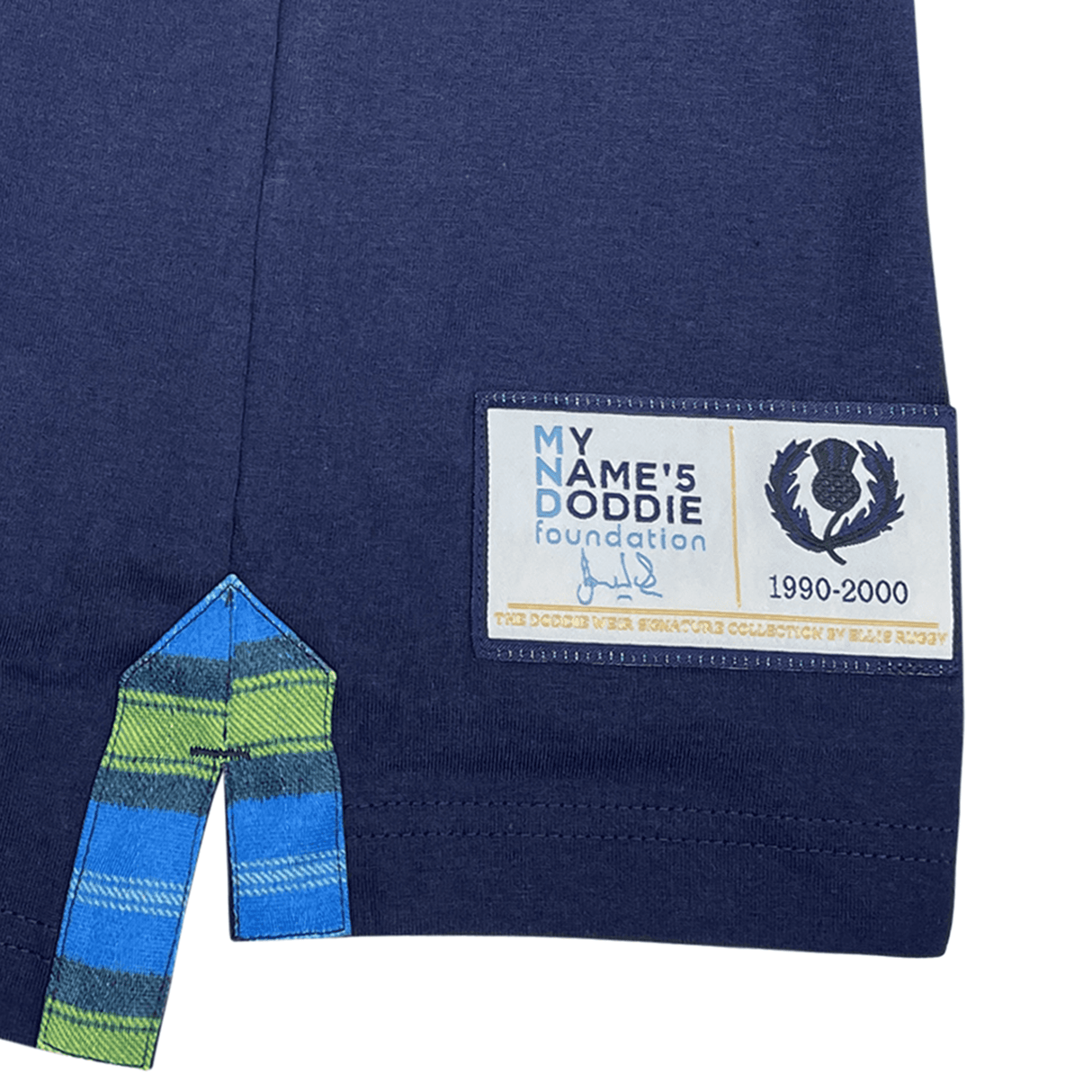 Close-up of a navy hem featuring "My Name'5 Doddie Foundation" label, logo, and "1990-2000." A green and blue plaid tartan trim at the bottom echoes the Ellis Rugby Doddie Weir Classic Jersey legacy.